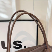 Borsa a spalla in pelle marrone con manici doppi, design elegante e moderno, ideale per moda donna. Sfondo bianco con cornice nera.