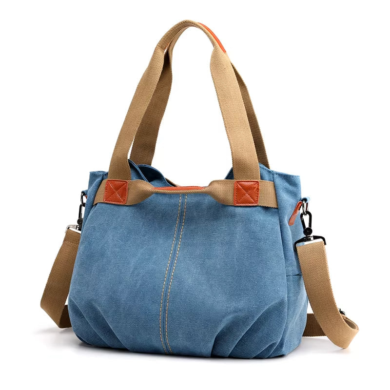 Borsa a tracolla in tela blu con manici beige, dettagli in pelle marrone, tasche laterali e tracolla regolabile. Stile casual, moda donna.