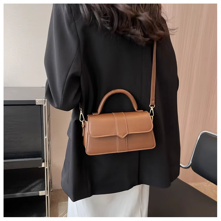 Donna con borsa a tracolla in pelle marrone, indossa giacca nera. Elegante accessorio moda, perfetto per look casual e formali.
