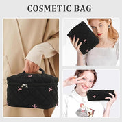 Borsa cosmetica nera trapuntata con cerniera, decorata con fiocchi rosa. Ideale per trucco, accessori viaggio. Donna che la tiene in mano.