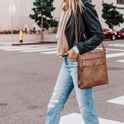 Donna con giacca in pelle nera, jeans strappati e borsa a tracolla marrone in pelle, attraversa la strada. Stile casual urbano, moda autunnale.