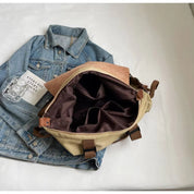 Zaino in tela beige aperto su giacca di jeans, con tasche interne visibili. Design casual, ideale per viaggi e uso quotidiano. Accessori moda uomo.