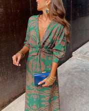 Donna con abito lungo verde a fantasia, accessori dorati e pochette blu. Moda elegante, abbigliamento femminile, tendenze 2023.