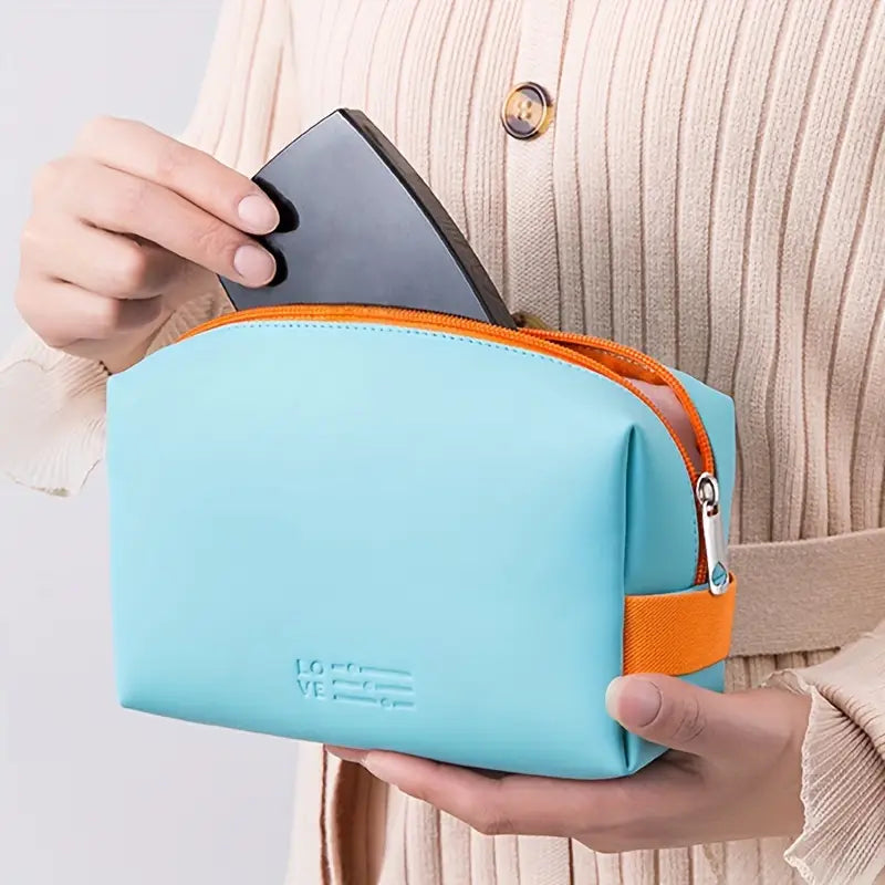 Donna inserisce smartphone in borsa da toilette azzurra con cerniera arancione. Accessorio da viaggio elegante e pratico.