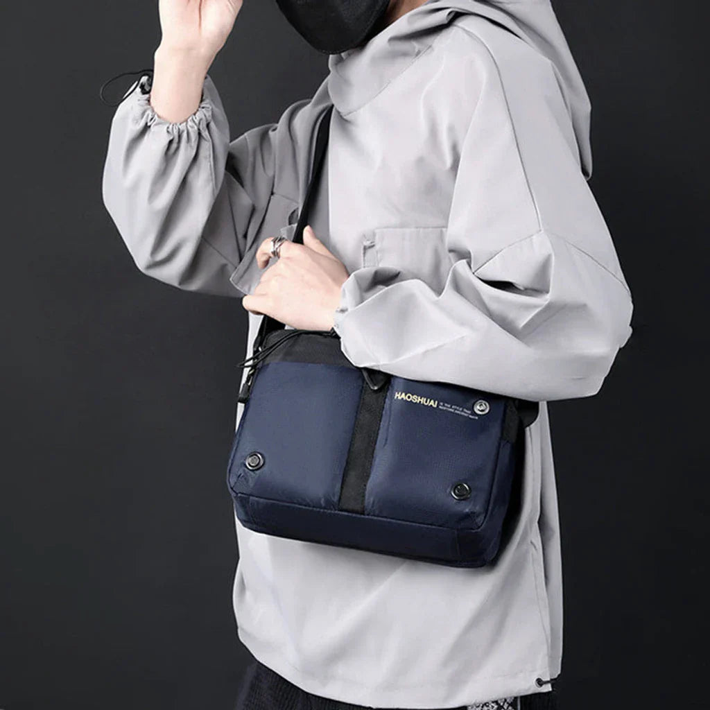 Giacca grigia con borsa a tracolla blu scuro, design moderno e funzionale, ideale per moda urbana e viaggi. Accessorio unisex, stile casual.