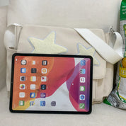 Borsa a tracolla beige con stelle applicate, tablet con schermo acceso davanti. Accessori moda donna, tecnologia, design moderno.