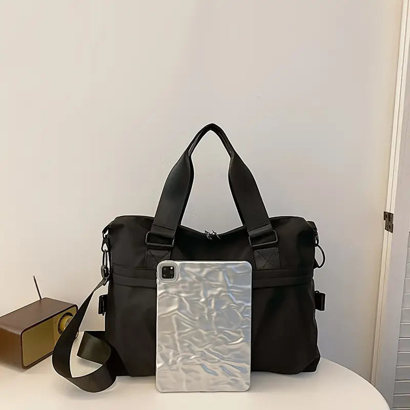 Borsa a tracolla nera elegante con manici, accanto a un tablet argento. Design moderno, ideale per lavoro e viaggio. Accessori moda unisex.