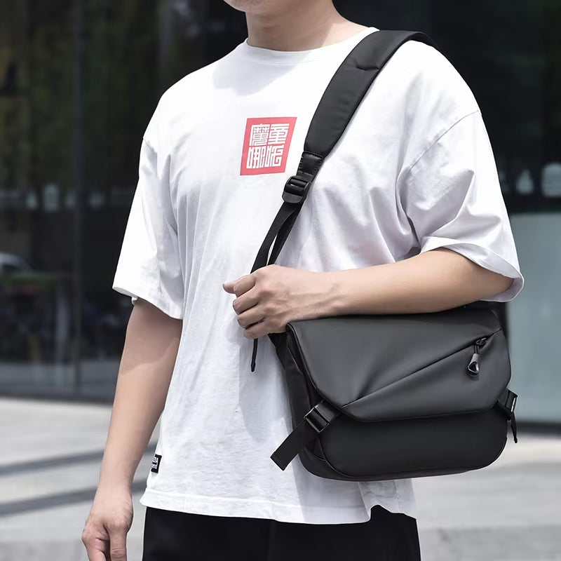 Uomo con borsa a tracolla nera in pelle, indossa maglietta bianca. Accessorio moda maschile, casual, urbano, perfetto per lavoro o viaggio.