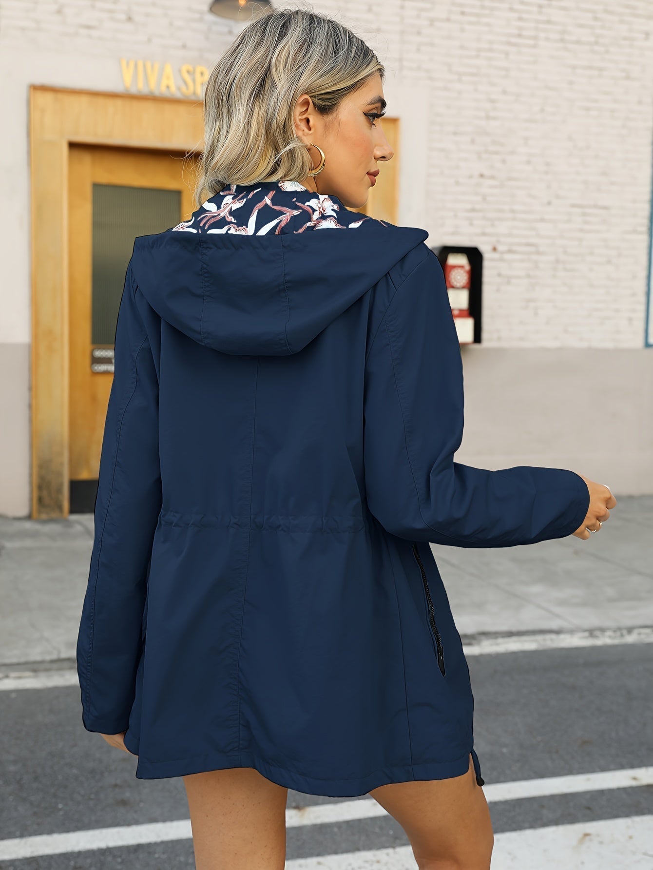 Donna con giacca a vento blu scuro con cappuccio, dettagli floreali, in strada urbana. Moda autunnale, abbigliamento casual femminile.