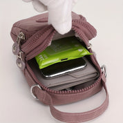 Borsa a tracolla rosa con zip aperta, contenente smartphone, portafoglio e salviette. Design compatto, ideale per viaggi e uso quotidiano.