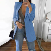 Donna con blazer azzurro, top grigio e jeans, scatta selfie in camera moderna. Moda casual elegante, abbigliamento femminile trendy.