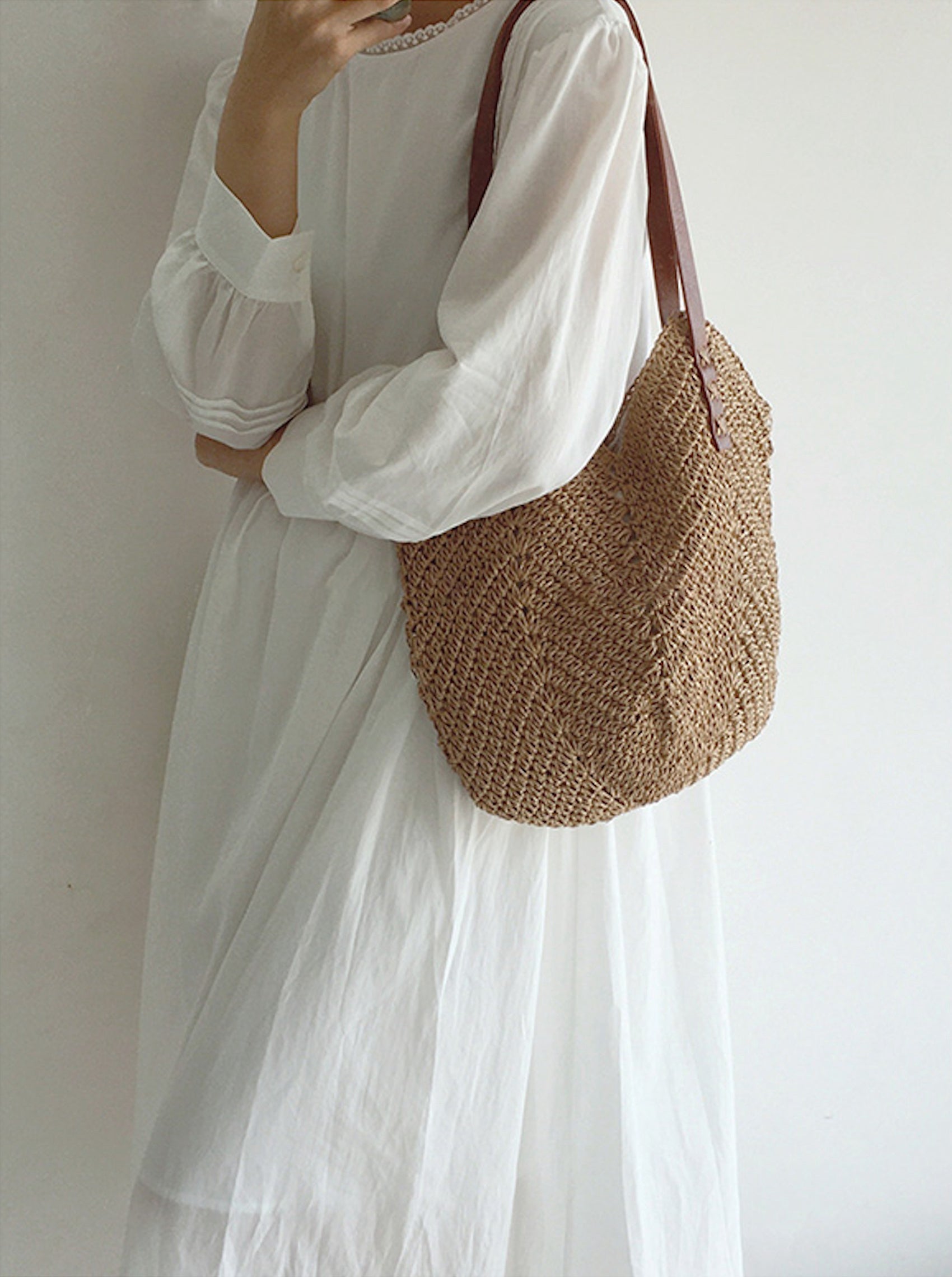 Donna con abito bianco lungo e borsa a tracolla in paglia intrecciata. Moda estiva, accessori eleganti, stile casual chic.