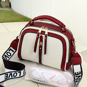 Borsa a tracolla bianca e bordeaux con cerniere dorate e manico superiore, tracolla regolabile con scritta "LOVE", su sfondo esterno moderno.