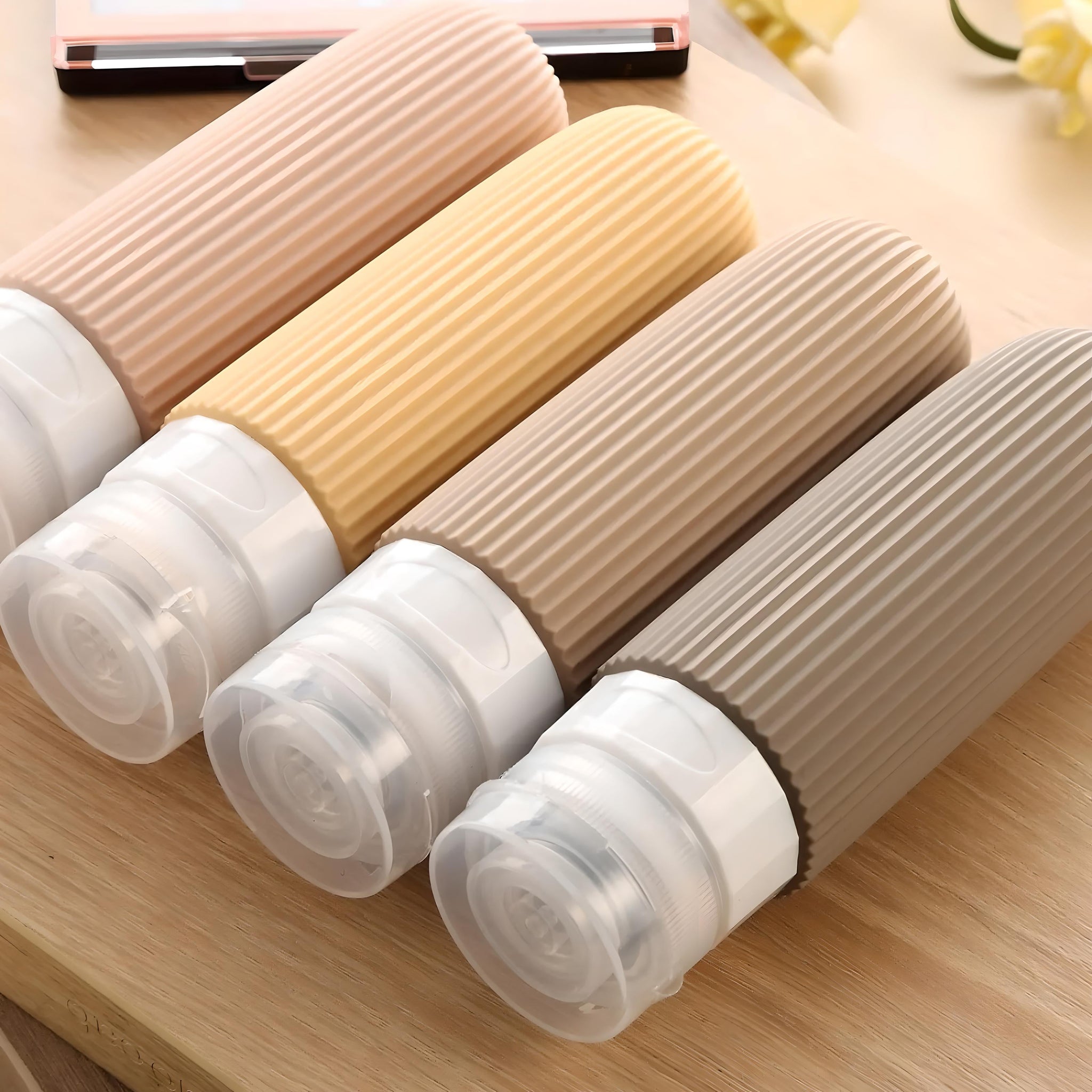 Quattro flaconi da viaggio in silicone colorati su tavola di legno, design pieghevole, ideali per shampoo e cosmetici. Accessori da viaggio pratici.