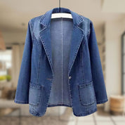 Giacca blazer in denim blu, stile casual, con tasche frontali, appesa su gruccia. Perfetta per look moda donna autunno-inverno.