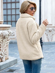 Giacca in pile beige donna, stile casual, indossata con jeans blu. Moda autunno inverno, look urbano elegante. Sfondo architettonico classico.