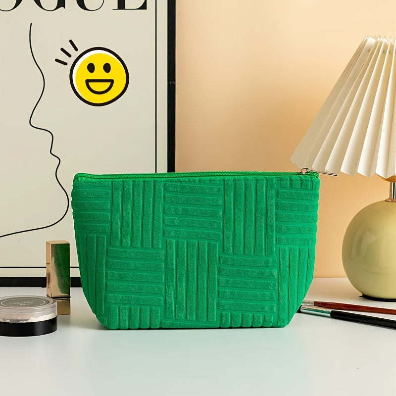 Borsa cosmetica verde con motivo geometrico, posizionata su un tavolo accanto a una lampada moderna e articoli di bellezza. Design elegante e funzionale.