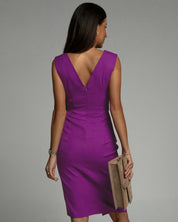 Abito viola senza maniche con scollo a V, indossato da donna di spalle, accessoriato con pochette beige. Elegante e moderno.