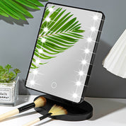 Specchio cosmetico LED rettangolare con foglia verde riflessa, base nera, pennelli trucco, decorazione moderna, illuminazione regolabile.