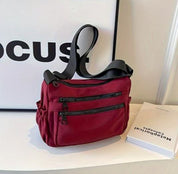 Borsa a tracolla rossa con cerniere nere su mensola bianca, accanto a libro e quadro. Accessorio moda donna, design elegante e pratico.
