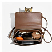 Borsa a tracolla marrone aperta con chiusura dorata, contenente rossetto, specchietto, portamonete e chiavi. Accessorio moda elegante e funzionale.