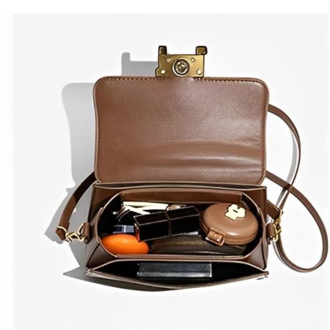 Borsa a tracolla marrone aperta con chiusura dorata, contenente rossetto, specchietto, portamonete e chiavi. Accessorio moda elegante e funzionale.