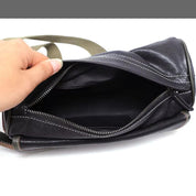 Borsa a tracolla in pelle nera aperta, con cerniera e cuciture bianche, tenuta da una mano. Design elegante e pratico per uso quotidiano.