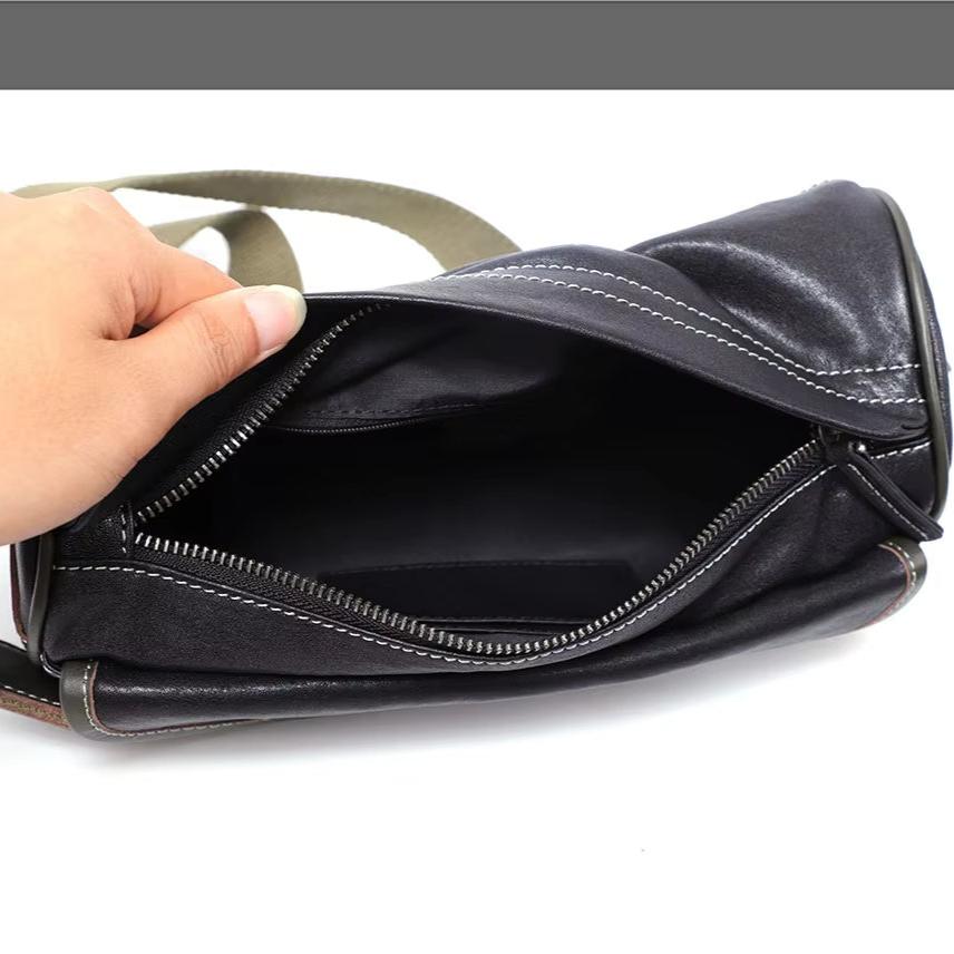 Borsa a tracolla in pelle nera aperta, con cerniera e cuciture bianche, tenuta da una mano. Design elegante e pratico per uso quotidiano.