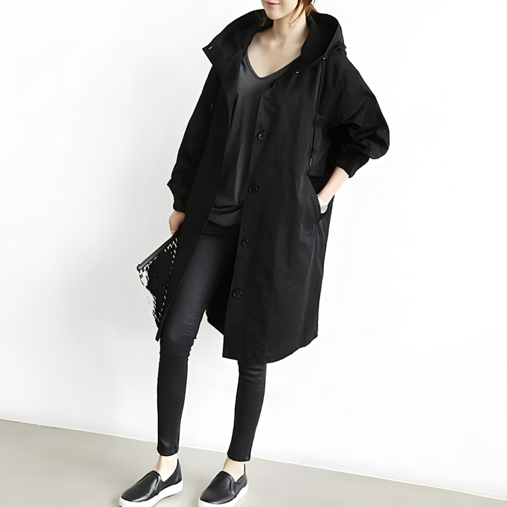 Donna con cappotto nero lungo, pantaloni aderenti e scarpe slip-on nere. Moda autunnale, abbigliamento casual chic, stile urbano minimalista.