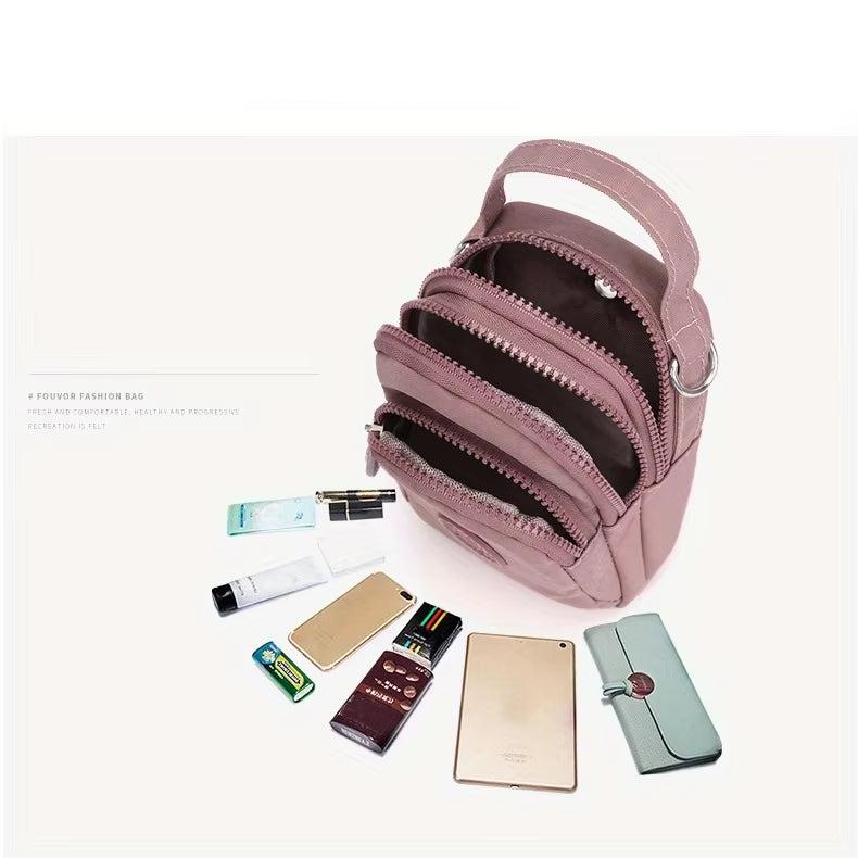 Zaino moda rosa con più scomparti aperti, circondato da oggetti quotidiani come smartphone, portafoglio e cosmetici. Accessorio elegante e pratico.