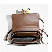 Borsa a tracolla in pelle marrone aperta, con chiusura dorata e scomparti interni, su sfondo bianco. Elegante accessorio moda donna.
