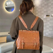 Zaino in pelle marrone su donna di spalle, design elegante con fibbie e borchie, perfetto per moda urbana e viaggi. Accessorio trendy e funzionale.