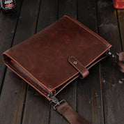 Borsa a tracolla in pelle marrone su tavolo di legno scuro, design elegante e resistente, ideale per lavoro e viaggio. Accessorio moda uomo.