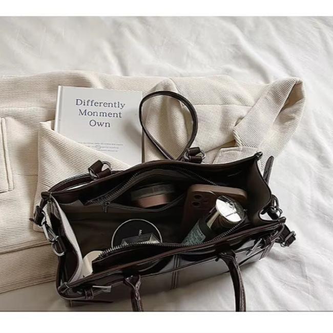 Borsa in pelle marrone su letto bianco, contenente libro, cosmetici e accessori. Elegante e pratica, ideale per moda e organizzazione quotidiana.