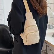 Zaino a tracolla beige in velluto a coste, indossato da una persona con cappotto nero. Design compatto, ideale per moda casual e viaggi urbani.
