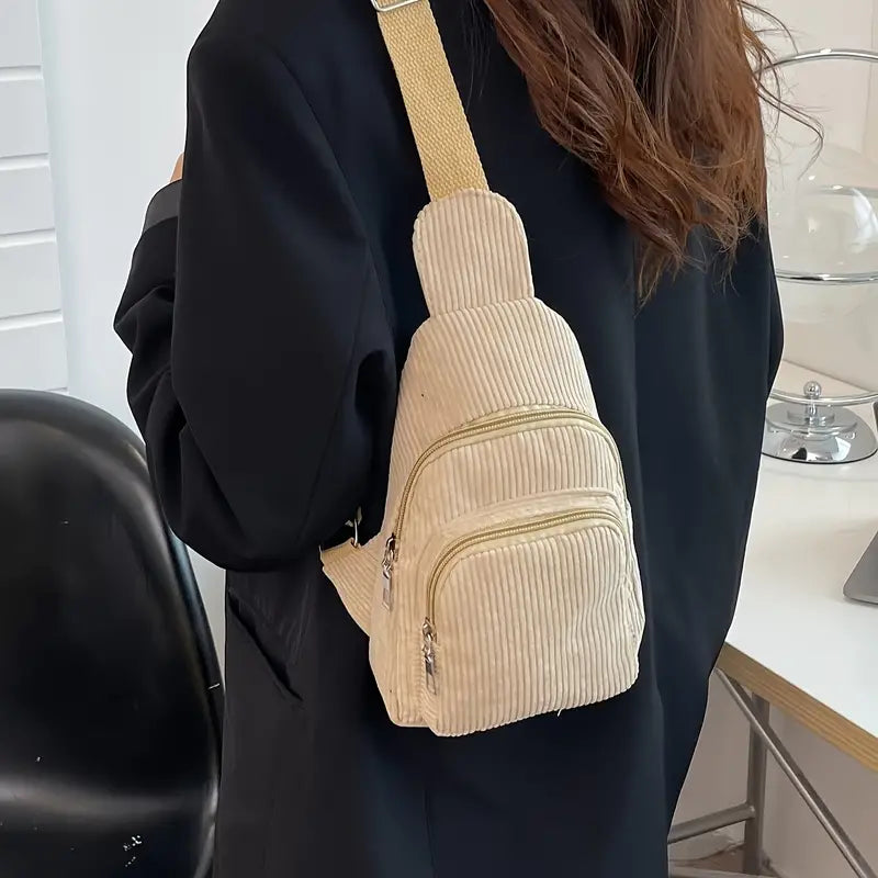 Zaino a tracolla beige in velluto a coste, indossato da una persona con cappotto nero. Design compatto, ideale per moda casual e viaggi urbani.