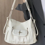 Borsa a tracolla bianca in pelle sintetica con dettagli a stella, tasca frontale con zip, indossata da una persona in abito grigio.