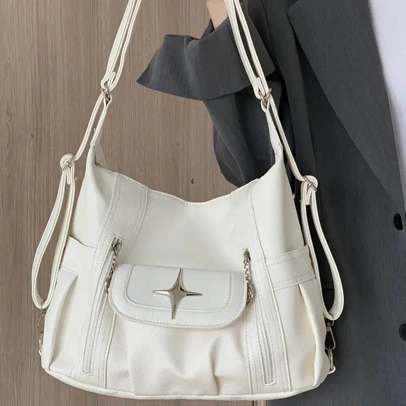 Borsa a tracolla bianca in pelle sintetica con dettagli a stella, tasca frontale con zip, indossata da una persona in abito grigio.