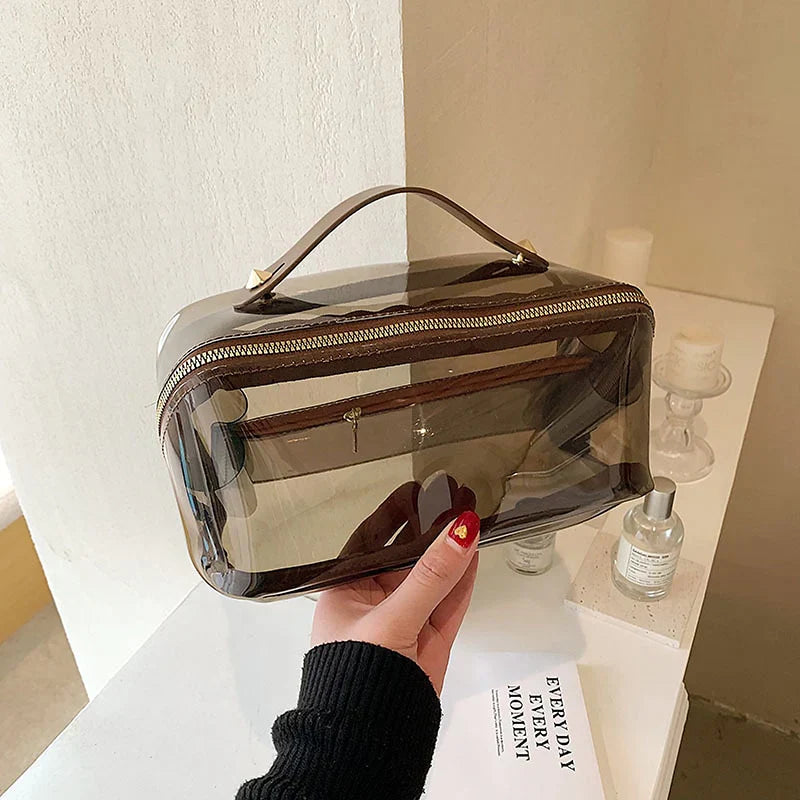 Borsa trasparente in PVC con manico marrone, design moderno, ideale per viaggi e cosmetici. Accessorio moda pratico e versatile.