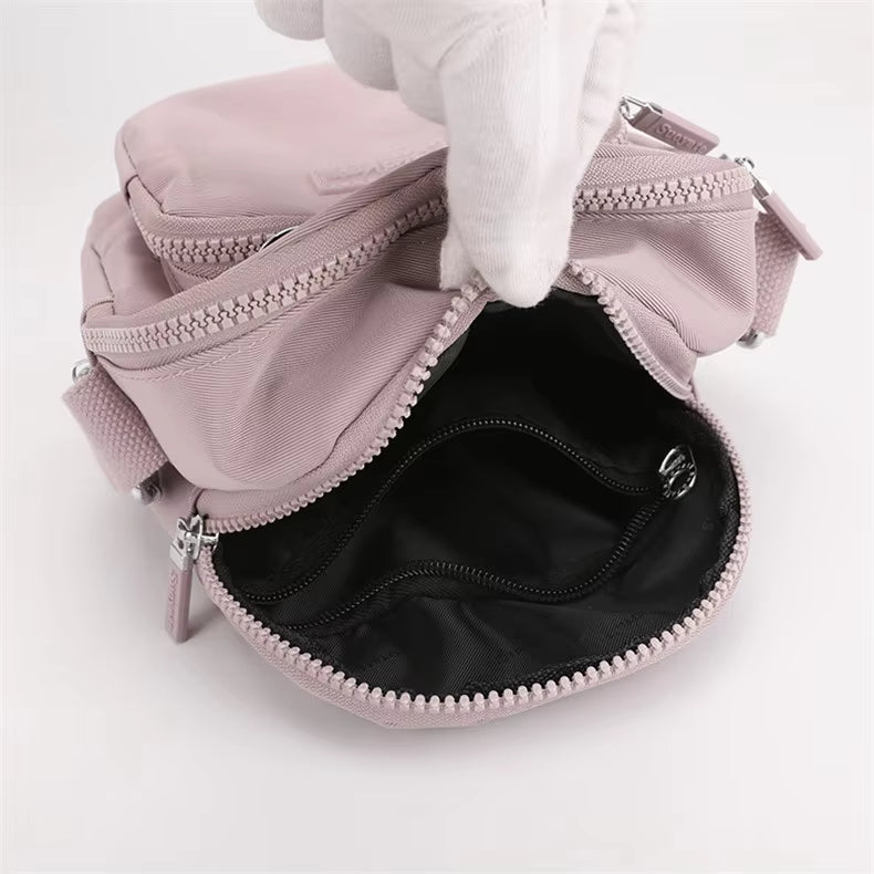Zaino compatto rosa con cerniere aperte, tasche multiple e design elegante. Ideale per moda femminile, accessori viaggio, borse casual.