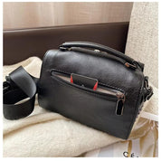 Borsa a tracolla in pelle nera su divano, con tasca frontale con zip e manico superiore. Design elegante, ideale per moda donna e accessori.