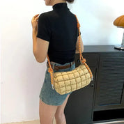 Donna con borsa a tracolla trapuntata beige, manico intrecciato arancione, indossa maglietta nera e gonna di jeans. Accessorio moda casual.