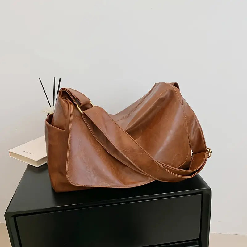 Borsa a tracolla in pelle marrone su mobile nero, design elegante e spazioso, ideale per viaggi e uso quotidiano. Accessorio moda versatile.