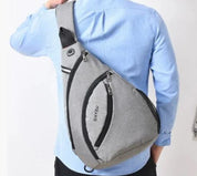 Uomo con zaino a tracolla grigio, design moderno, chiusura a zip, indossa camicia azzurra. Accessorio moda pratico e versatile.