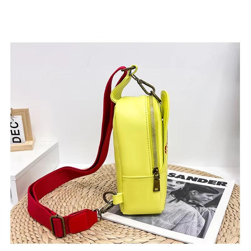 Borsa a tracolla gialla con cerniera, cinturino rosso regolabile, su tavolo con rivista e decorazione. Accessorio moda donna elegante e colorato.