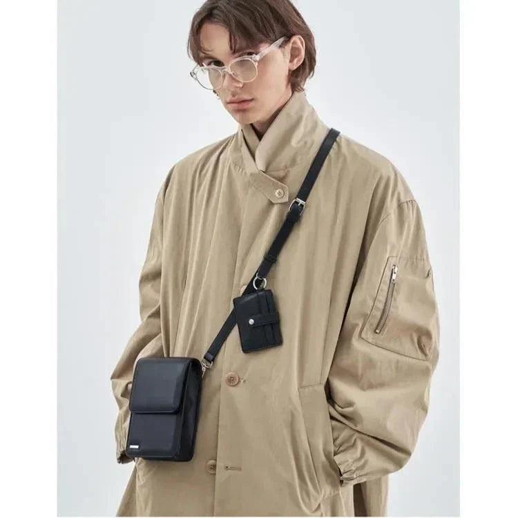Giovane con cappotto beige e occhiali trasparenti, indossa una borsa a tracolla nera. Moda uomo, accessori eleganti, stile contemporaneo.