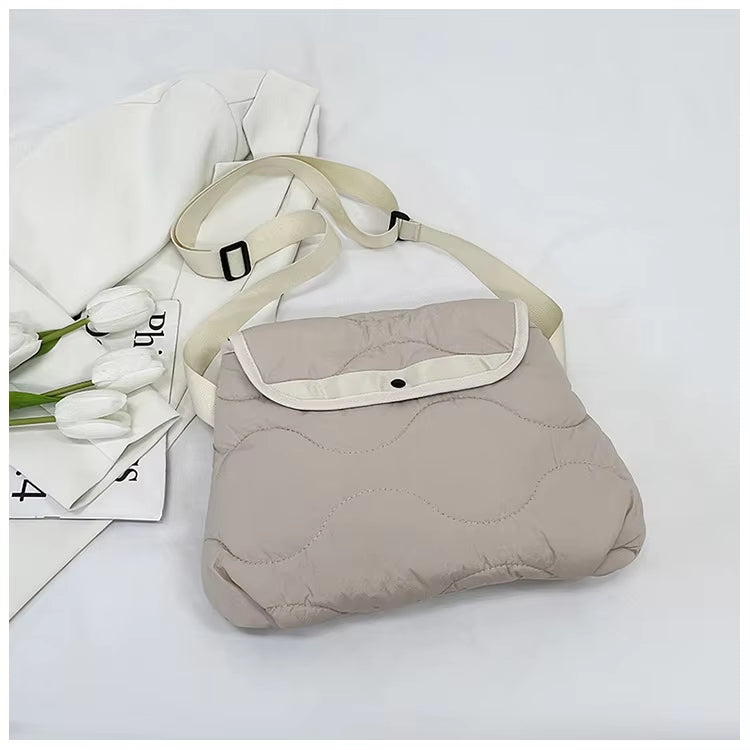 Borsa a tracolla imbottita beige con patta, cinturino regolabile e chiusura a bottone, su sfondo bianco con tulipani e rivista.