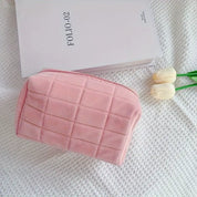 Astuccio rosa in velluto su coperta bianca, accanto a libro e tulipani. Elegante e morbido, ideale per cosmetici. Accessorio moda femminile.
