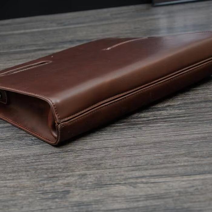 Custodia in pelle marrone per laptop su tavolo in legno, design elegante e sottile, ideale per protezione e trasporto sicuro di dispositivi elettronici.