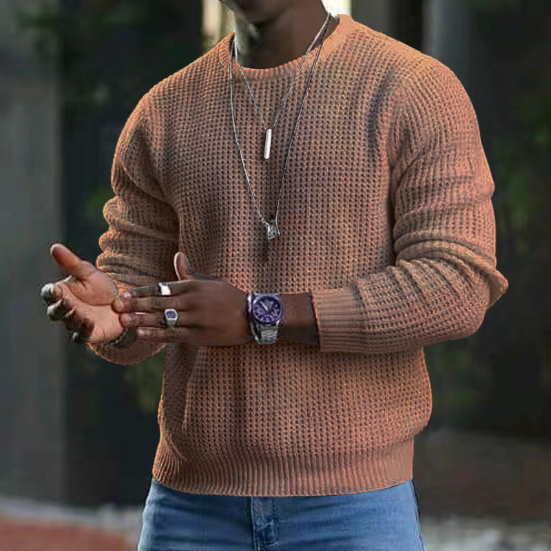 Maglione uomo marrone a maglia grossa, indossato con jeans blu. Accessori: orologio sportivo, collane e anelli. Moda casual autunnale.